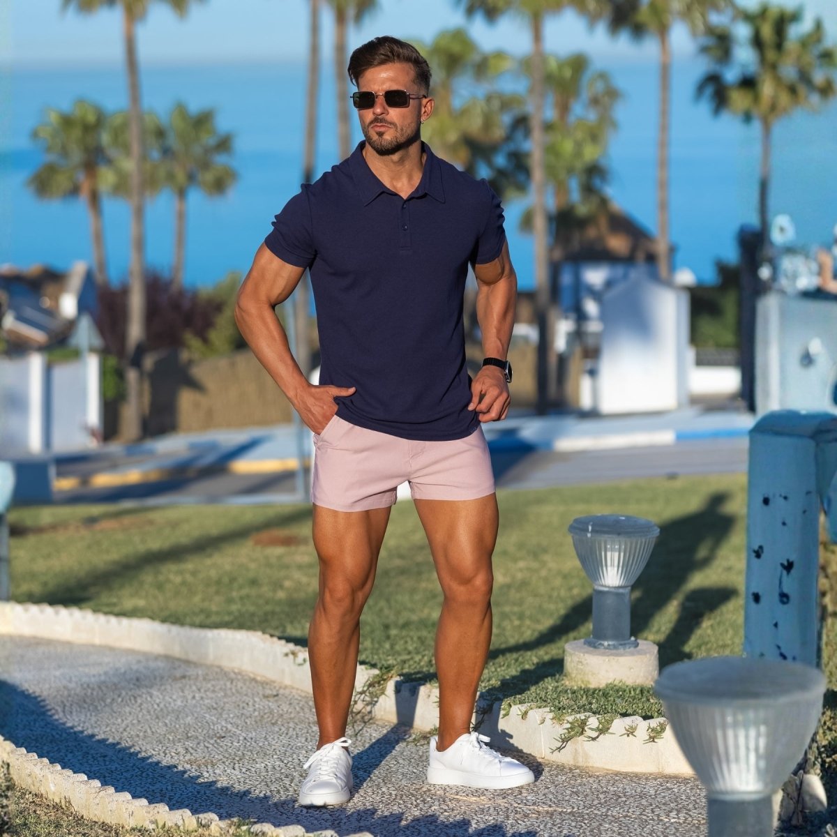 man wearing stylish smart casual outfit with navy blue slim fit polo and very short shorts in light pink